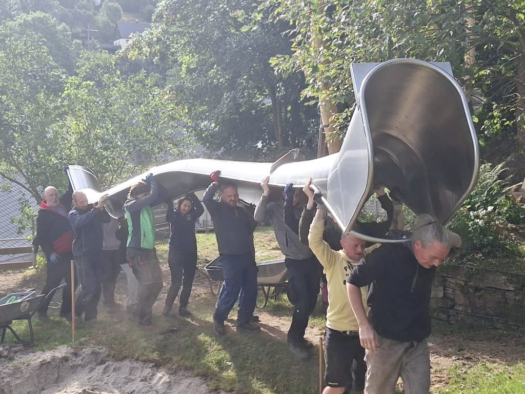 In 4 Elterneinsätzen gelang es uns, eine 7 Meter lange Rutsche, 19 Robinen Stämme mit bis zu 5 Meter Länge, einen Rutschen Aufstieg, der 7 Meter lang ist, und Tonnen von Beton und Sand mit Schubkarren und Minibagger an Ort und Stelle zu bringen.